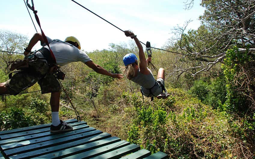A tour guide helps a girl to jump of the canopy tour platform.